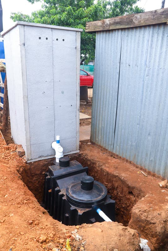 The Bio-Separator chamber seated in its trench alongside a completed toilet structure, with inlet pipework and access covers connected